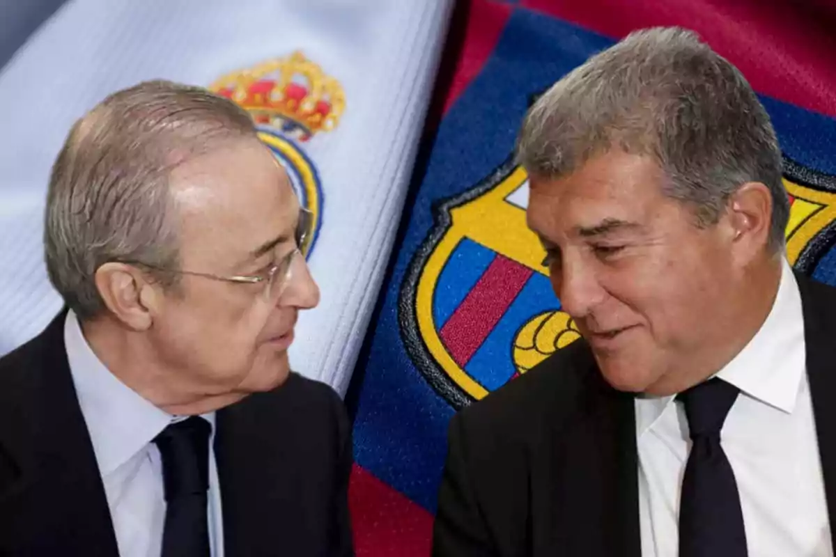 Dos hombres de traje conversando frente a los escudos de dos equipos de fútbol.