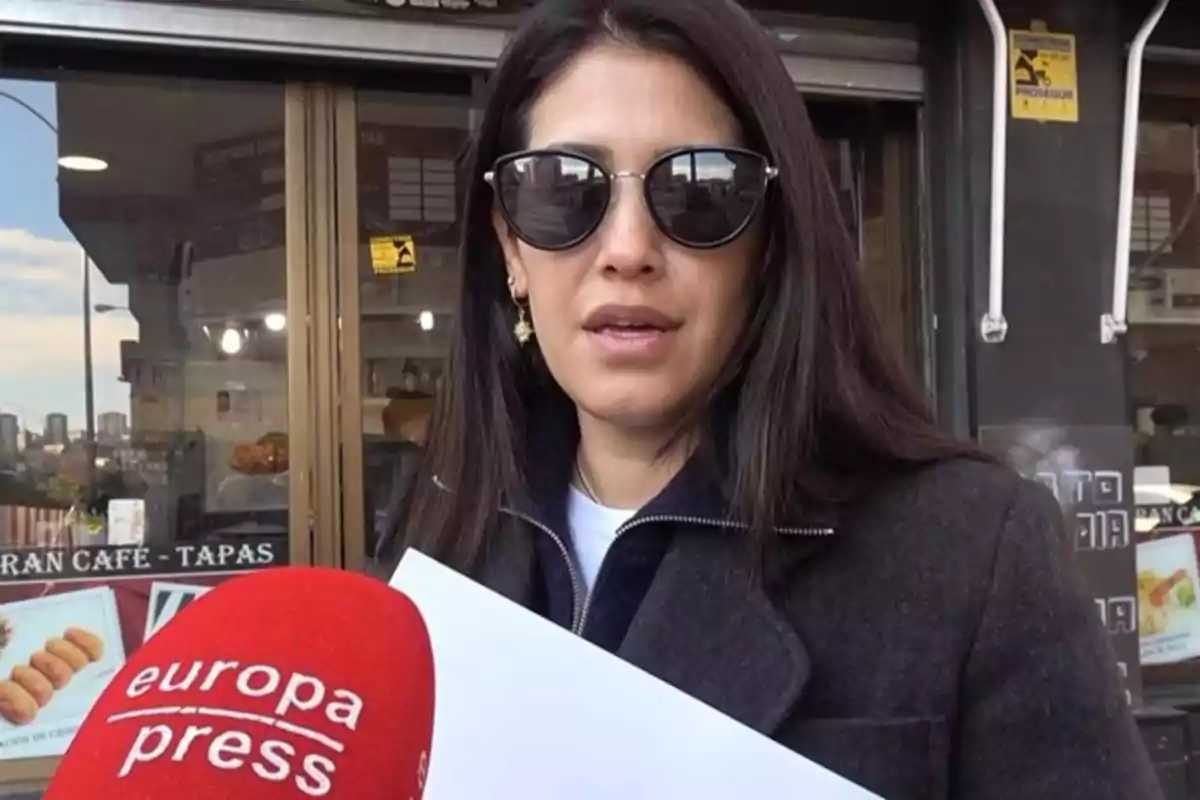 Una mujer con gafas de sol es entrevistada frente a un café, sosteniendo un papel y un micrófono de Europa Press. Una mujer con gafas de sol es entrevistada frente a un café, sosteniendo un papel y un micrófono de Europa Press.
