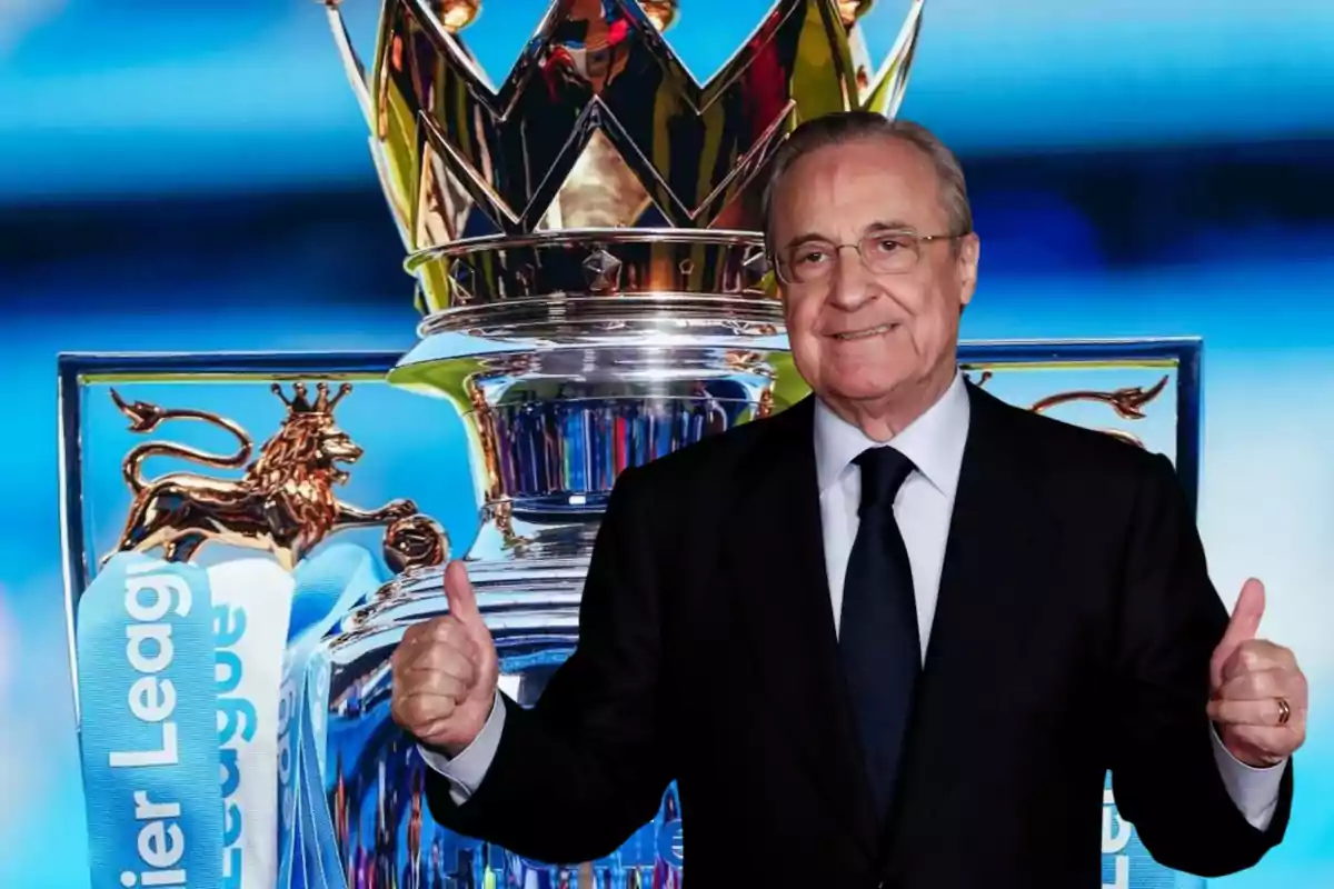 Un hombre con traje y corbata sonríe y levanta ambos pulgares frente a un trofeo de la Premier League.