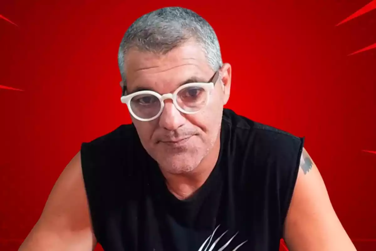 Hombre con gafas blancas y camiseta negra sobre fondo rojo.