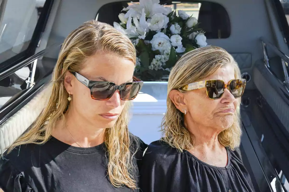 Dos mujeres con gafas de sol, vestidas de negro, están de pie frente a un ataúd adornado con flores blancas.