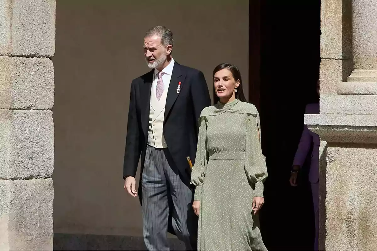 Una pareja elegantemente vestida camina junto a una pared de piedra. Una pareja elegantemente vestida camina junto a una pared de piedra.