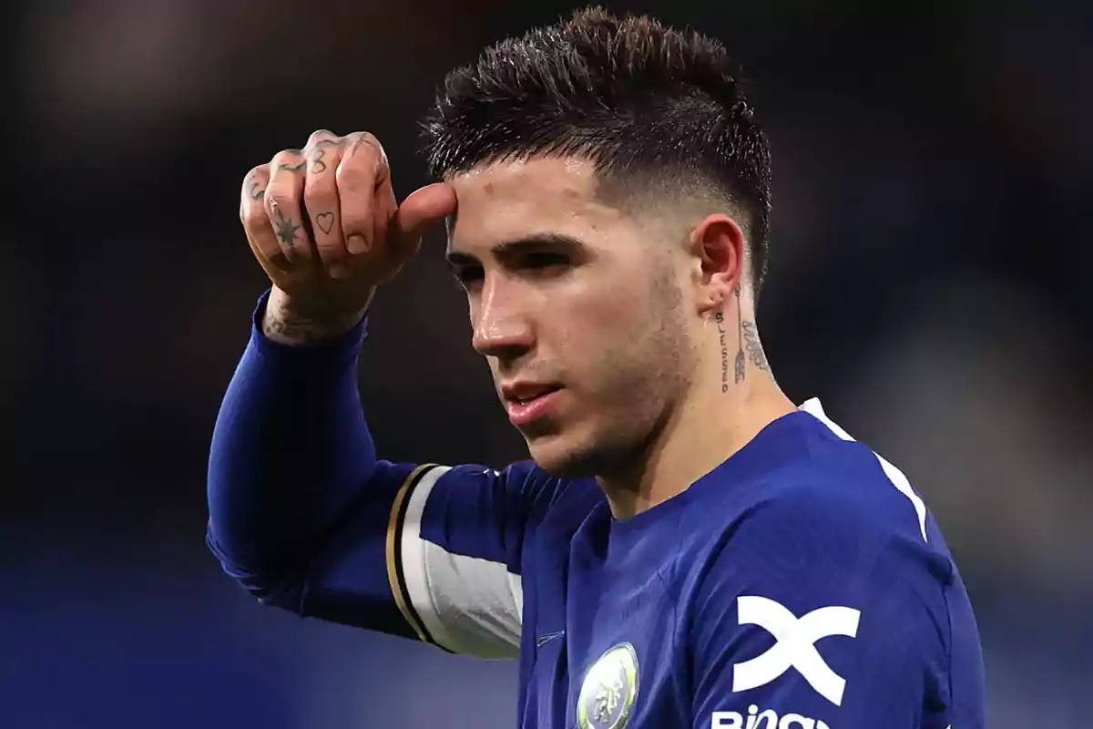 Un jugador de fútbol con uniforme azul se limpia el sudor de la frente durante un partido.