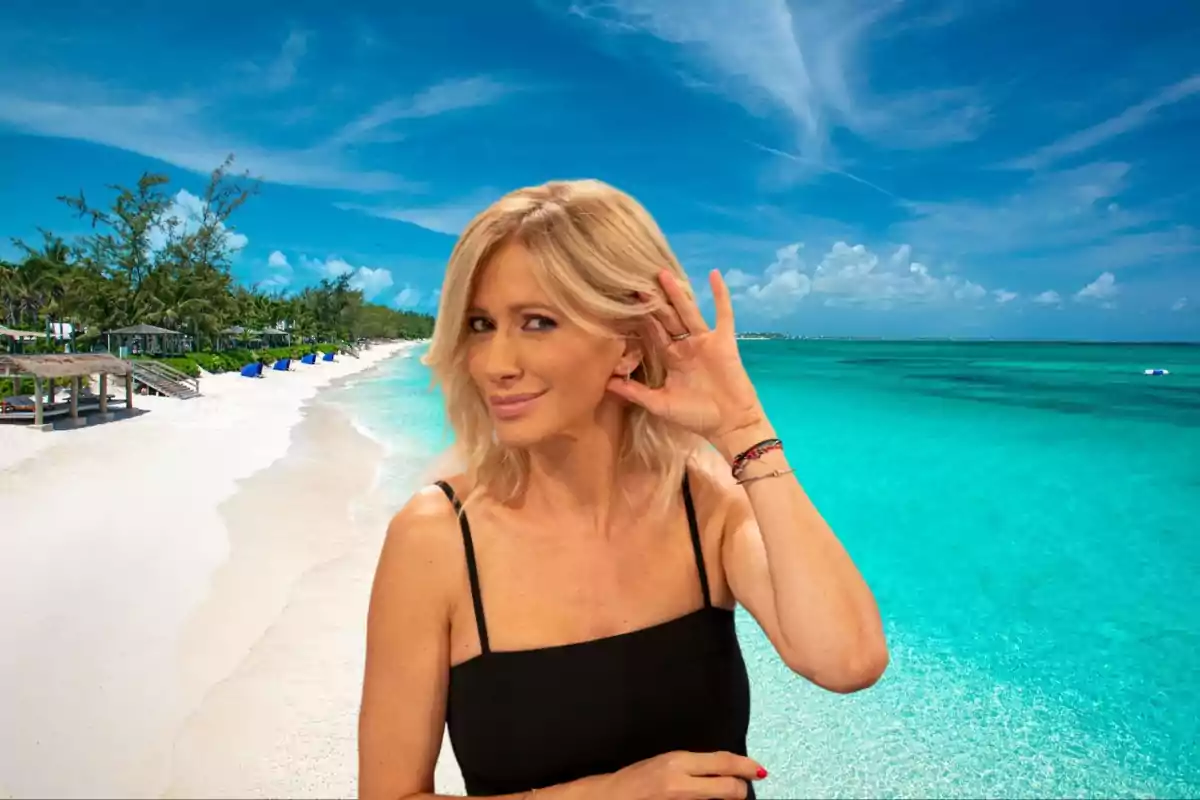 Una mujer rubia con vestido negro posando en una playa de arena blanca y mar turquesa bajo un cielo azul.