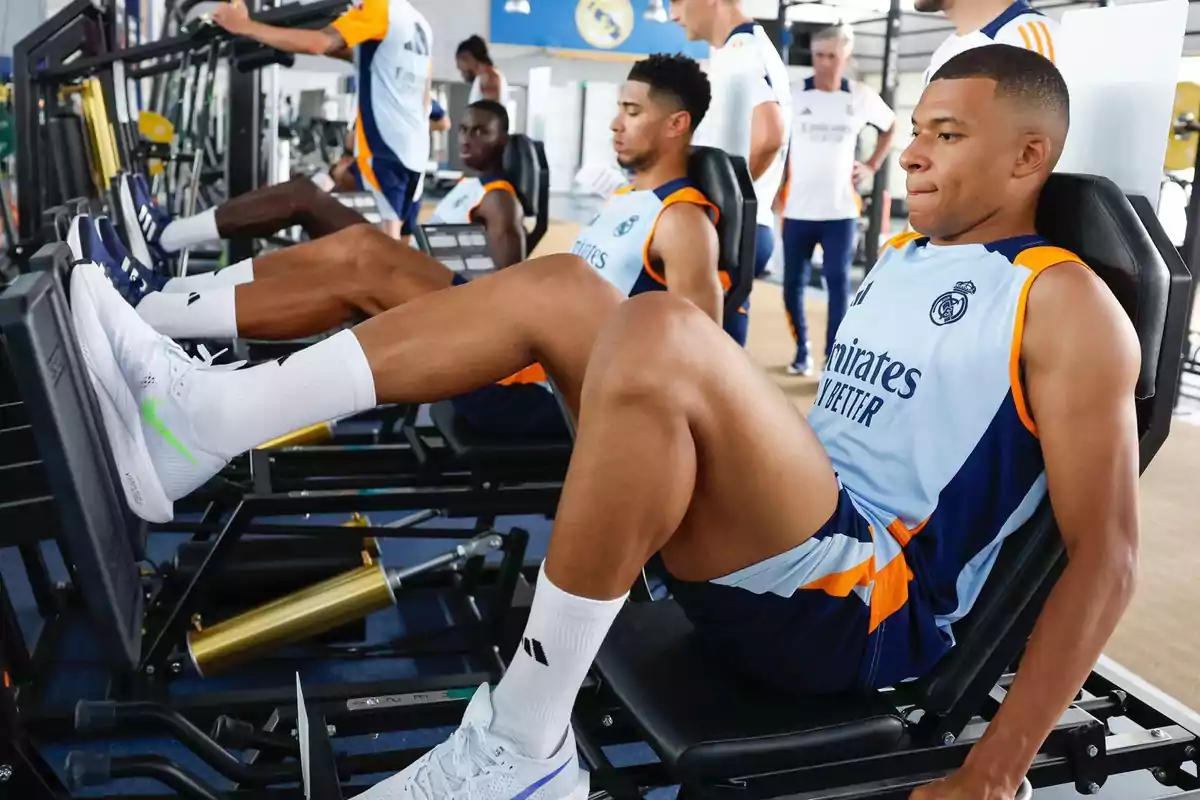 Jugadores de fútbol entrenando en el gimnasio usando máquinas de ejercicios para piernas.