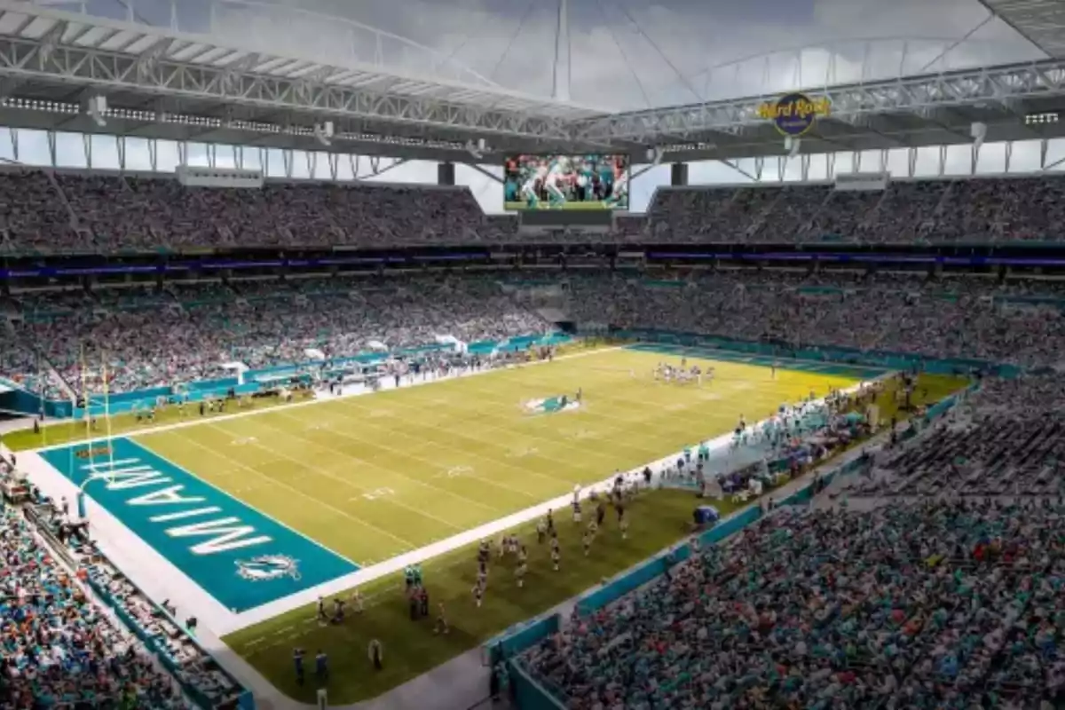 Estadio de fútbol americano lleno de aficionados durante un partido con el campo decorado con los colores y el logo de los Miami Dolphins Estadio de fútbol americano lleno de aficionados durante un partido con el campo decorado con los colores y el logo de los Miami Dolphins