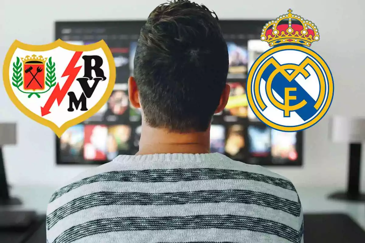 Un hombre de espaldas mirando una pantalla con los escudos del Rayo Vallecano y el Real Madrid.