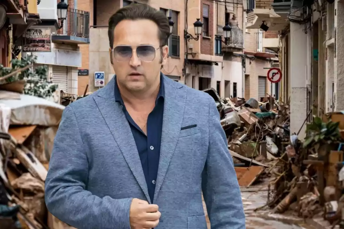 Un hombre con gafas de sol y chaqueta azul camina por una calle llena de escombros y basura.