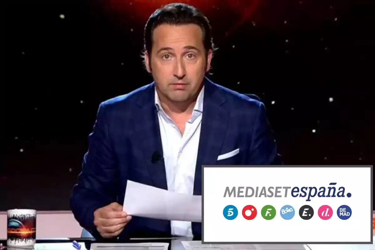 Un hombre con traje azul sostiene un papel mientras está sentado en un escritorio con una taza y bolígrafos. En la esquina inferior derecha aparece el logo de Mediaset España con varios iconos de canales.