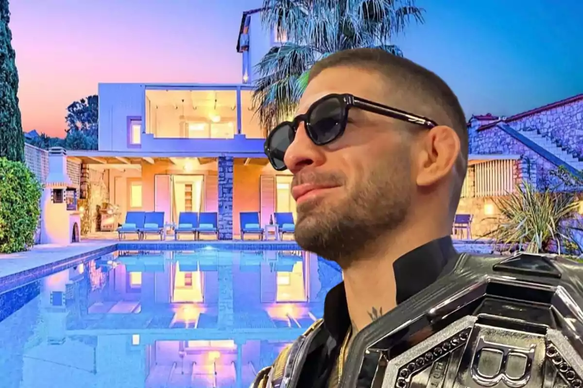 Hombre con gafas de sol y chaqueta con detalles metálicos frente a una casa moderna con piscina iluminada al atardecer.