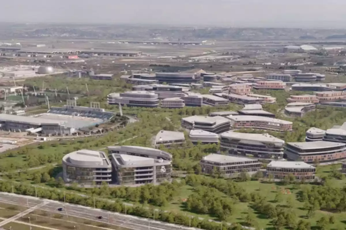 Vista aérea de un complejo de edificios modernos rodeados de áreas verdes y caminos, con un paisaje urbano y montañoso al fondo. Vista aérea de un complejo de edificios modernos rodeados de áreas verdes y caminos, con un paisaje urbano y montañoso al fondo.