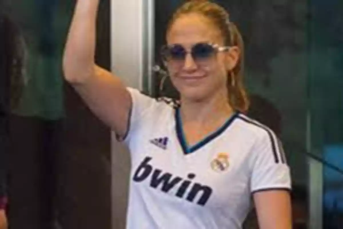 Mujer con gafas de sol y camiseta de fútbol blanca levantando el brazo.