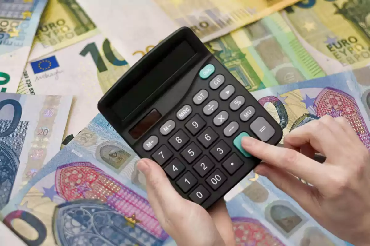 Una persona usando una calculadora sobre billetes de euro.