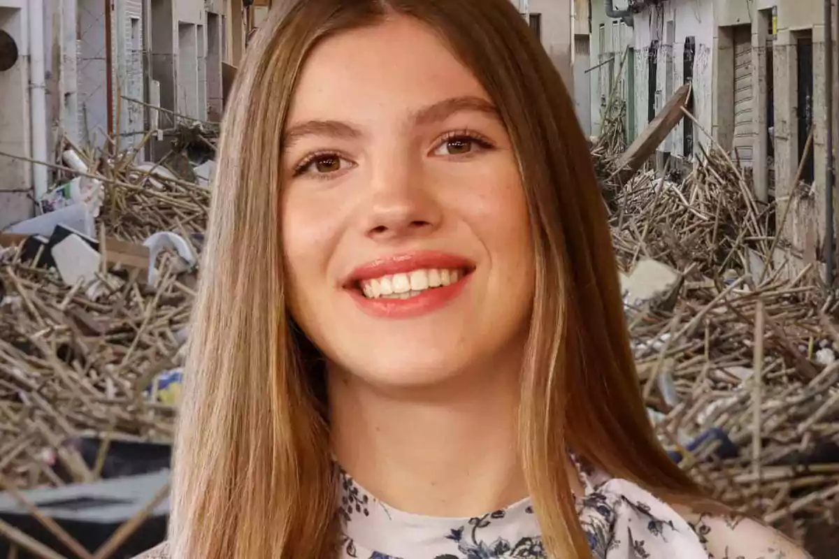 Una persona sonriente frente a un fondo de escombros en una calle.