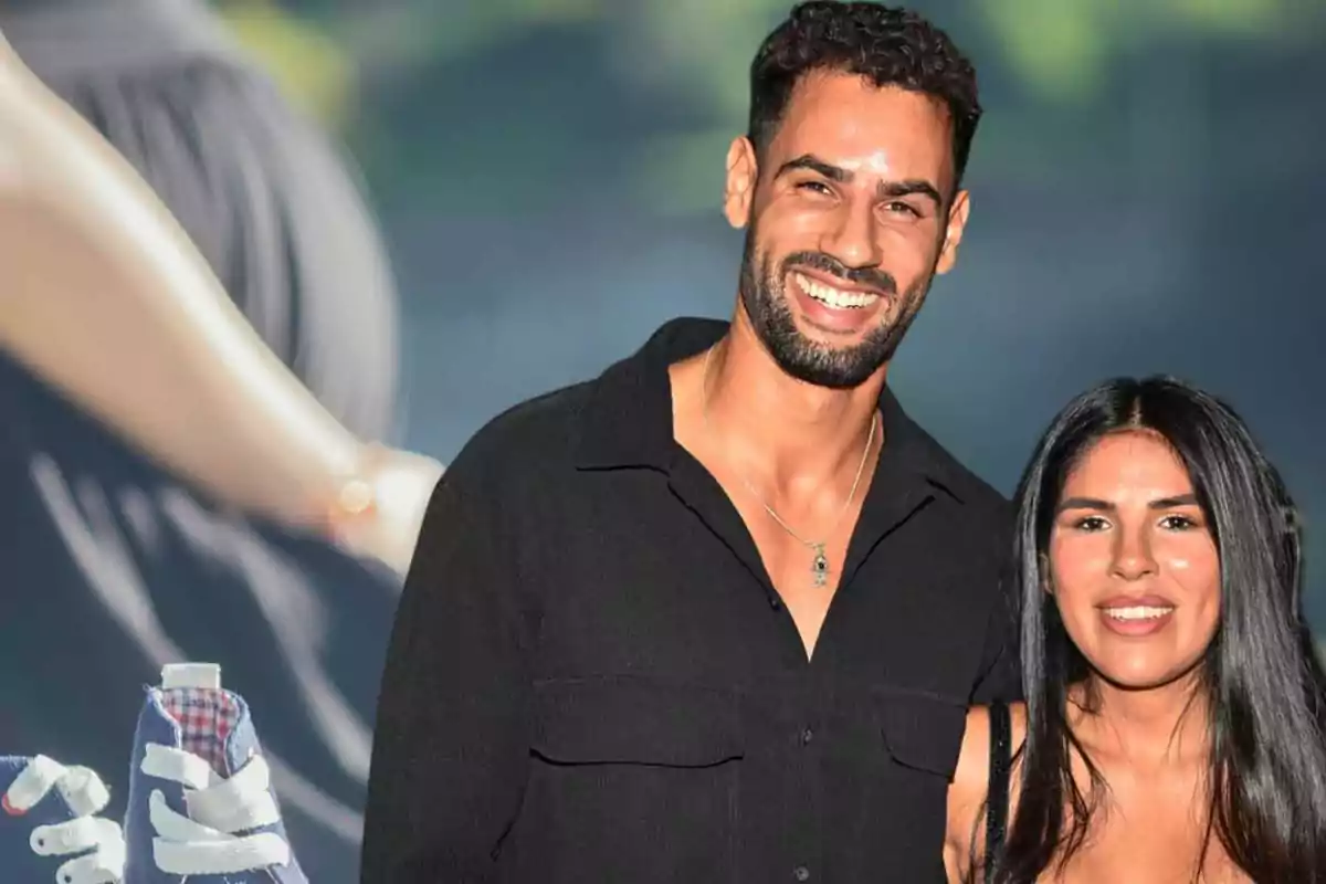 Una pareja sonriente posando frente a un fondo borroso con un par de zapatillas de bebé en primer plano.