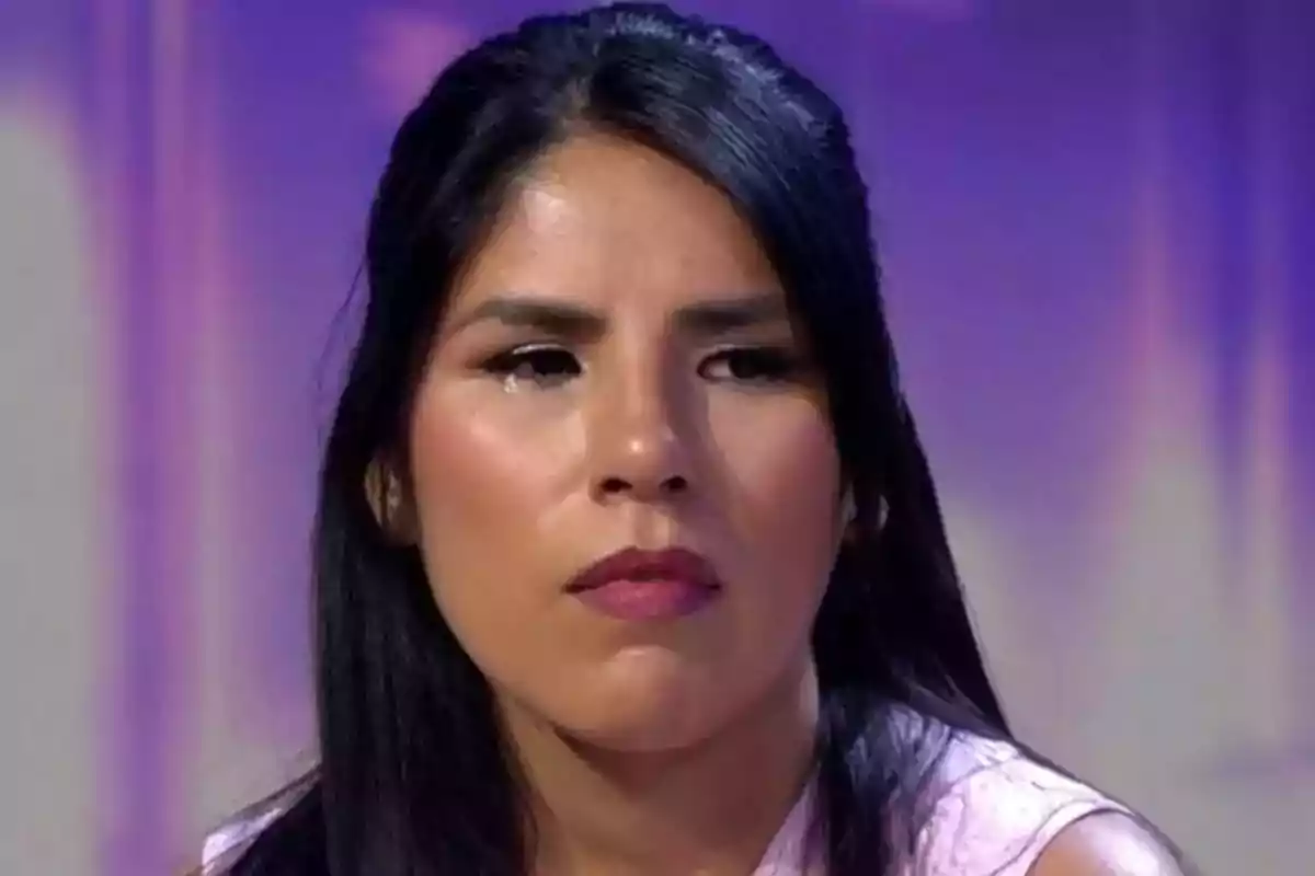 Mujer con expresión seria y lágrimas en el rostro en un fondo púrpura.