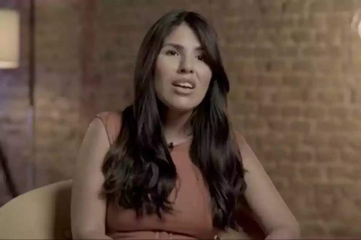 Mujer con cabello largo y oscuro sentada frente a una pared de ladrillos.