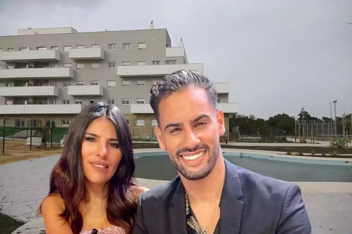 Una pareja sonriente posa frente a un edificio moderno con balcones y una piscina en primer plano.