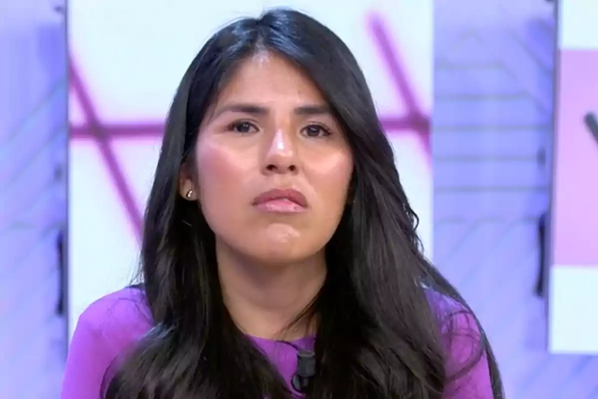 Mujer con cabello largo y oscuro vistiendo una blusa morada en un entorno de estudio de televisión.