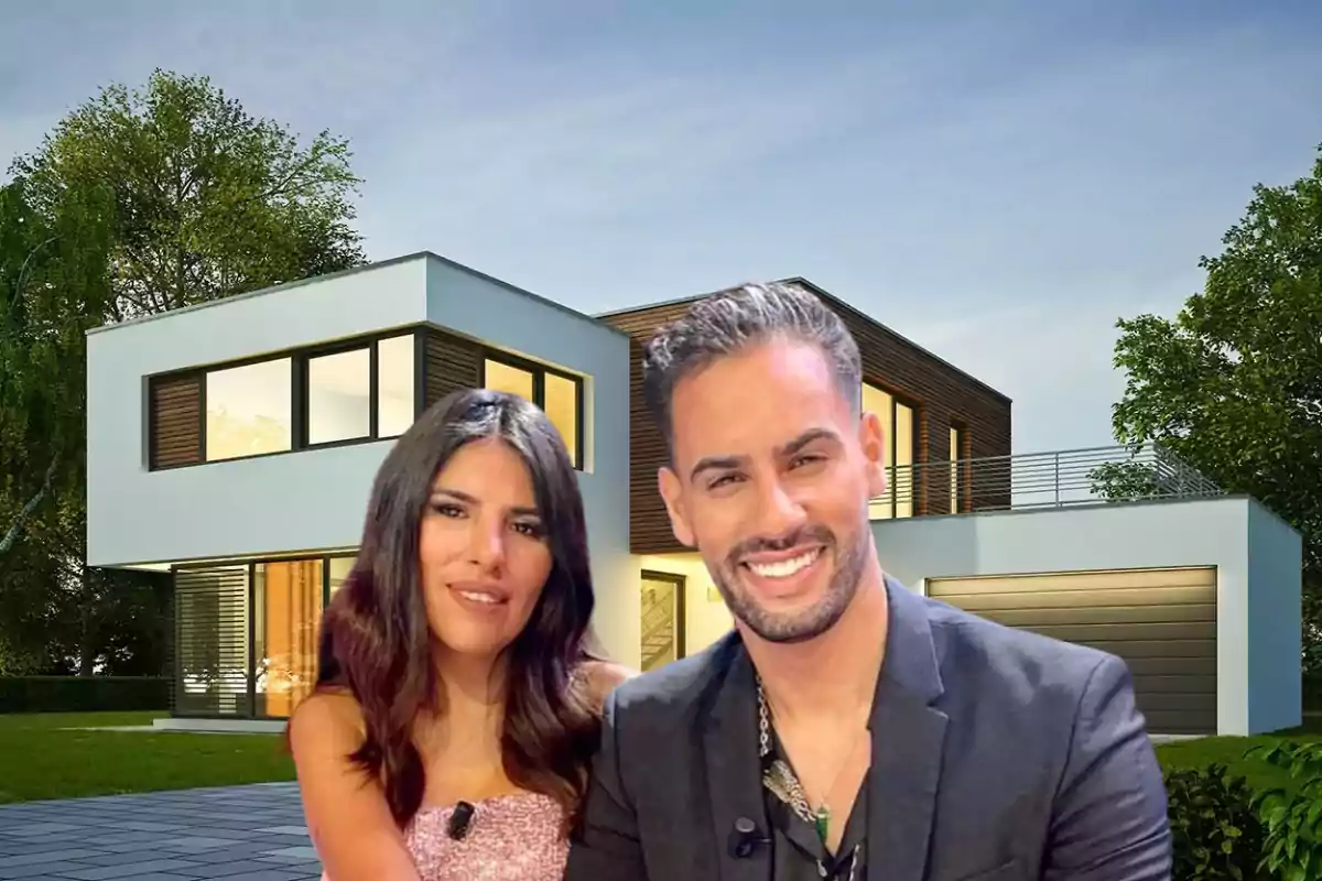 Una pareja sonriente posando frente a una casa moderna de dos pisos con grandes ventanas y rodeada de árboles.