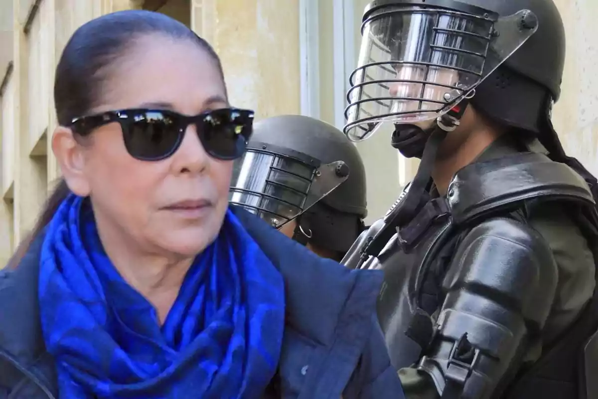 Mujer con gafas de sol y bufanda azul frente a policías antidisturbios con cascos y viseras.