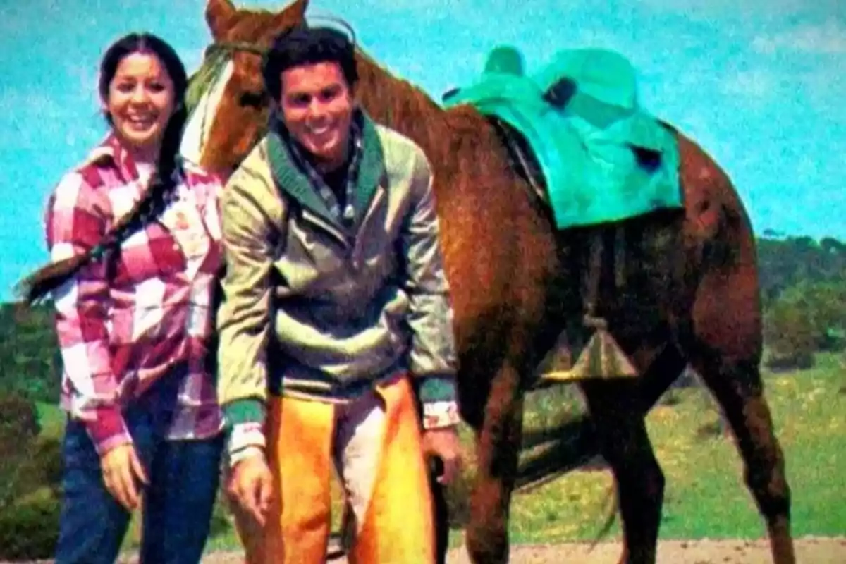 Una pareja sonriente posando junto a un caballo con una silla de montar verde. Una pareja sonriente posando junto a un caballo con una silla de montar verde.