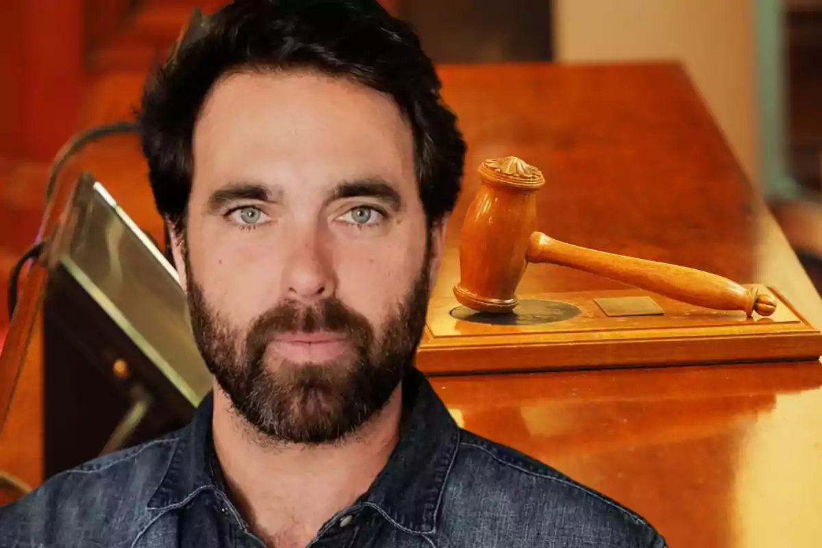 Un hombre con barba y cabello oscuro está frente a un mazo de juez sobre una mesa de madera.