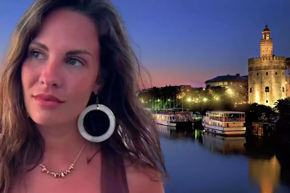 Una mujer con grandes pendientes y un collar posa frente a un paisaje nocturno con una torre iluminada y barcos en el agua.