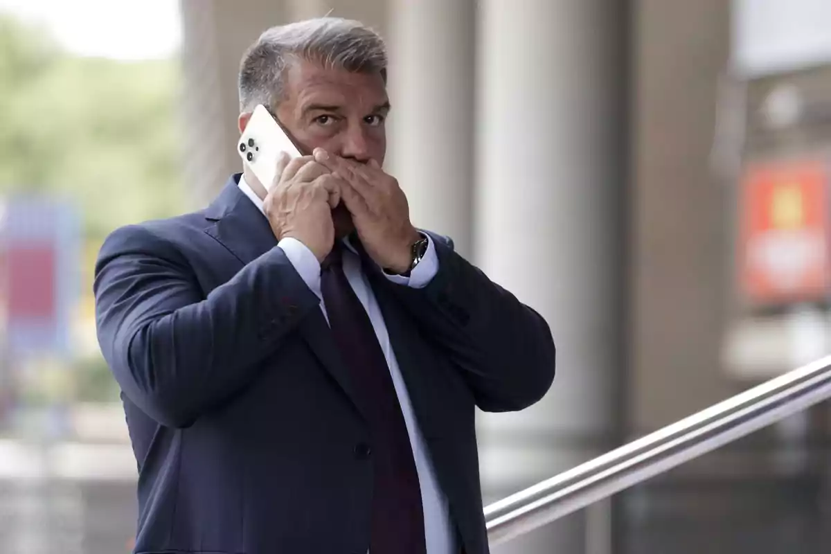 Hombre de traje hablando por teléfono móvil y cubriéndose la boca con la mano.