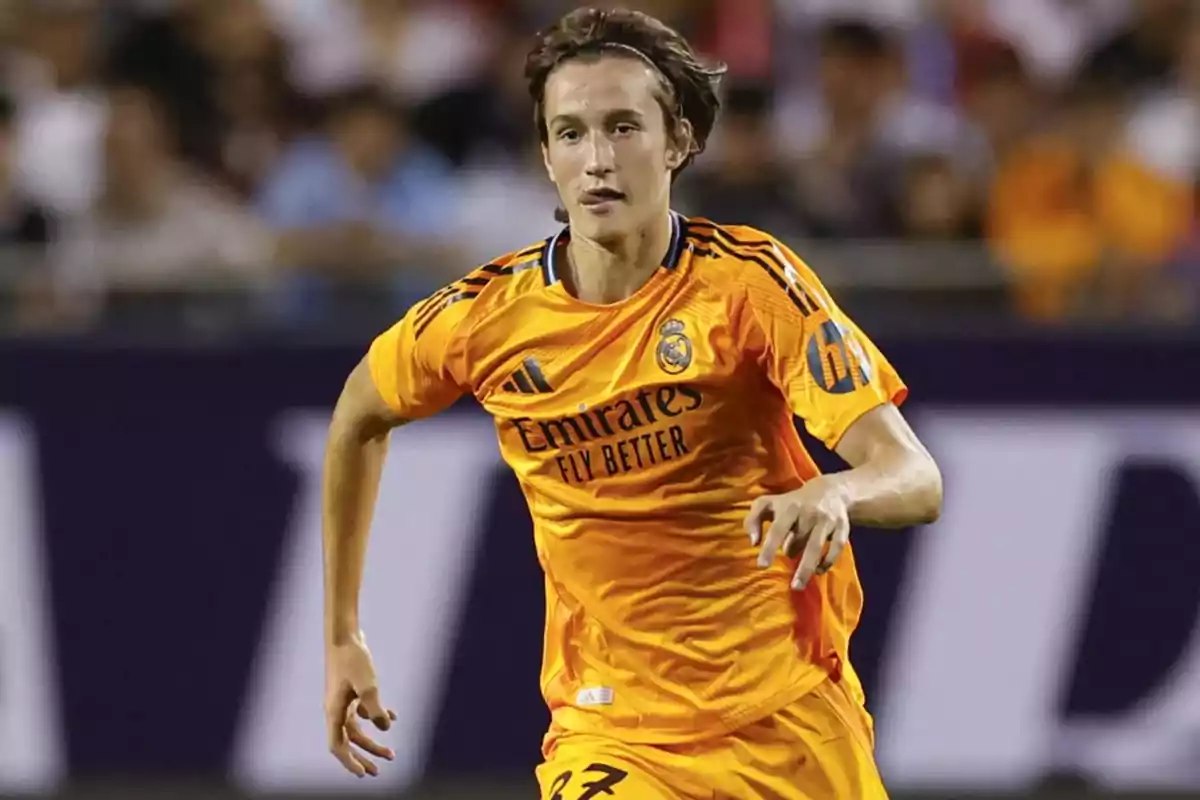 Jugador de fútbol con uniforme naranja del Real Madrid en acción durante un partido. Jugador de fútbol con uniforme naranja del Real Madrid en acción durante un partido.
