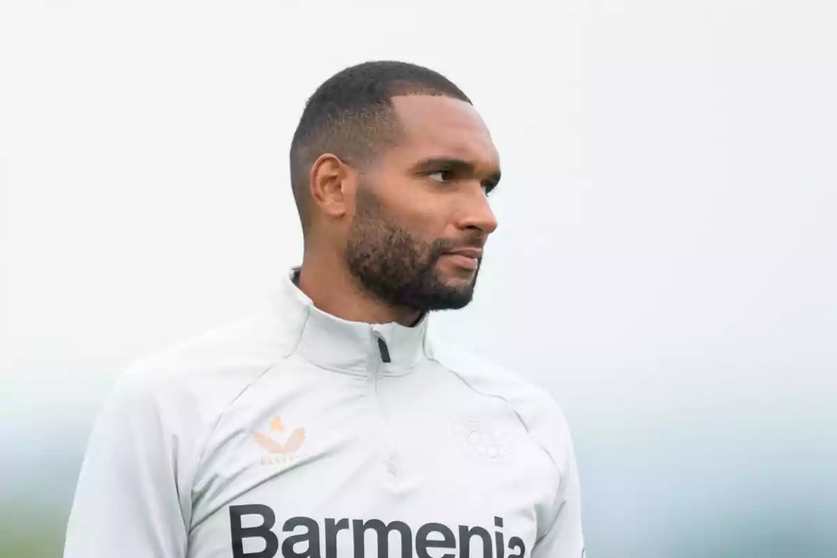 Hombre con barba y cabello corto vistiendo una chaqueta deportiva blanca con logotipos.