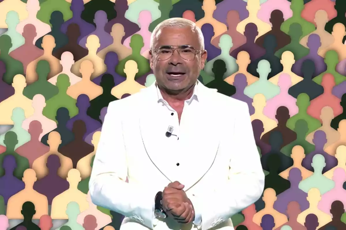 Un hombre con gafas y cabello corto canoso, vestido con un traje blanco, está de pie frente a un fondo colorido con siluetas de personas en diferentes colores.