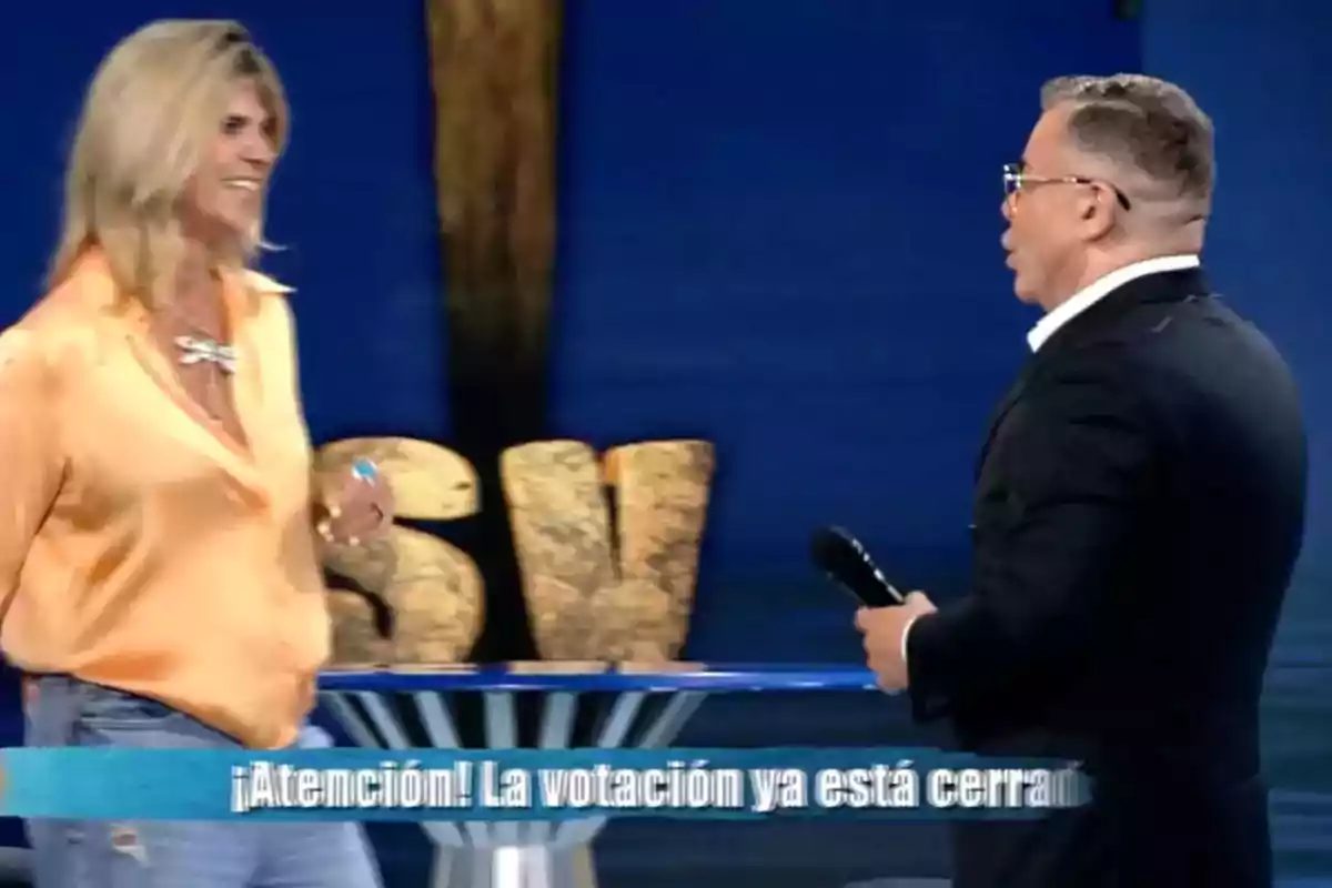 Dos personas conversan en un set de televisión con letras grandes de fondo y un mensaje en la parte inferior que indica que la votación ya está cerrada Dos personas conversan en un set de televisión con letras grandes de fondo y un mensaje en la parte inferior que indica que la votación ya está cerrada