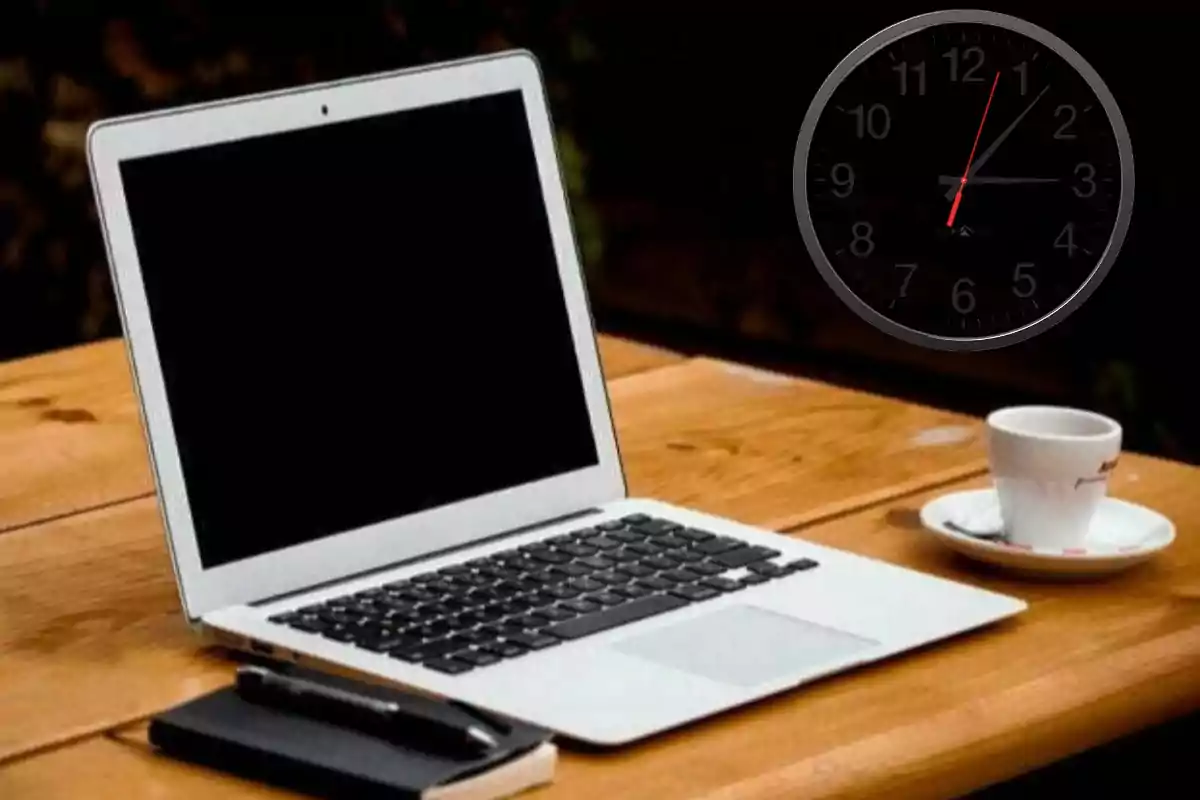 Una laptop sobre una mesa de madera junto a una taza de café y un reloj de pared.