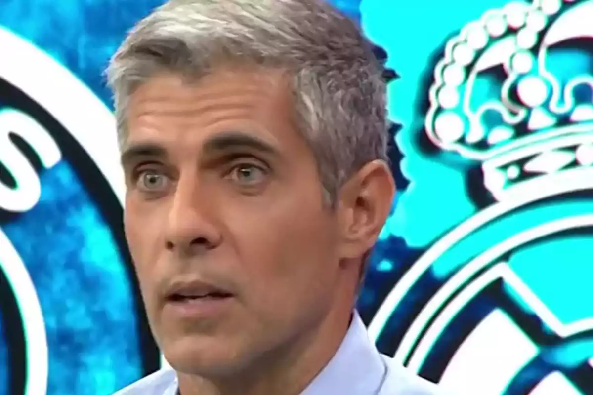 Un hombre de cabello canoso y expresión seria con un fondo azul y un logotipo. Un hombre de cabello canoso y expresión seria con un fondo azul y un logotipo.