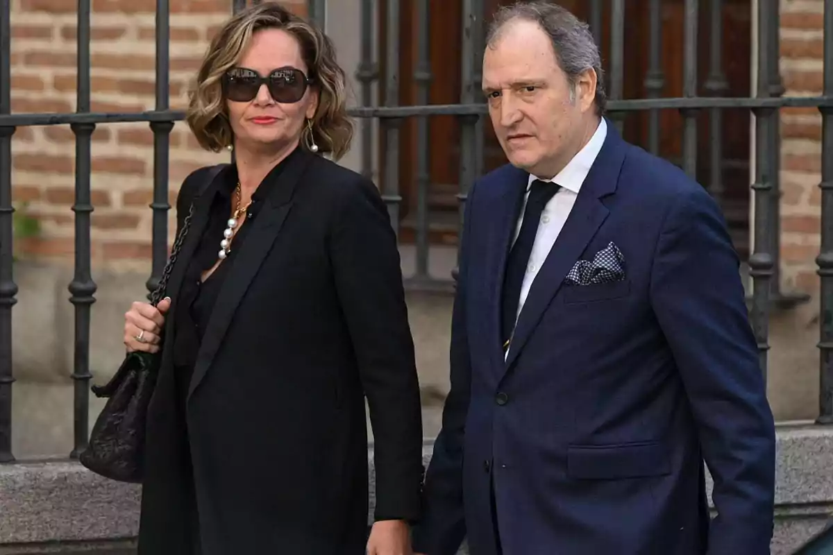 Una mujer y un hombre vestidos formalmente caminando juntos frente a una reja de hierro. Una mujer y un hombre vestidos formalmente caminando juntos frente a una reja de hierro.