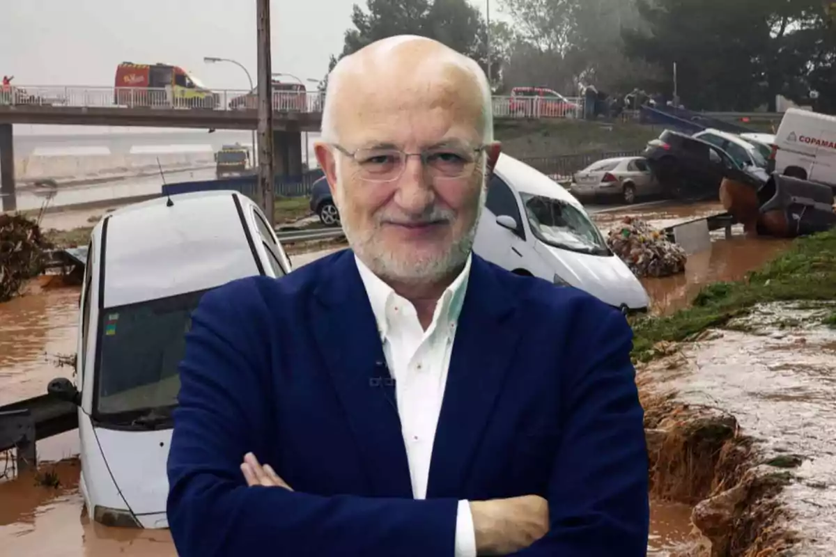 Un hombre de pie con los brazos cruzados frente a una escena de inundación con autos dañados y agua en la carretera.