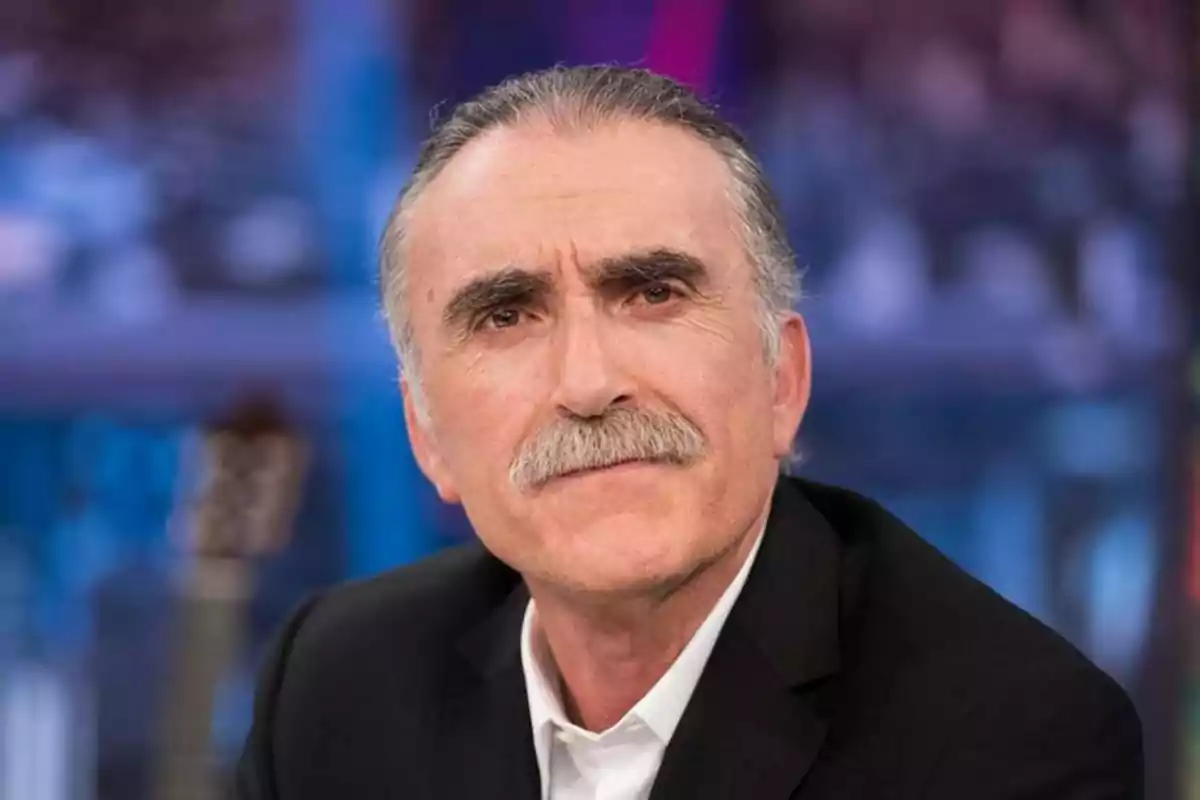 Un hombre de cabello canoso y bigote, vestido con traje oscuro y camisa blanca, mira hacia la cámara con expresión seria. Un hombre de cabello canoso y bigote, vestido con traje oscuro y camisa blanca, mira hacia la cámara con expresión seria.