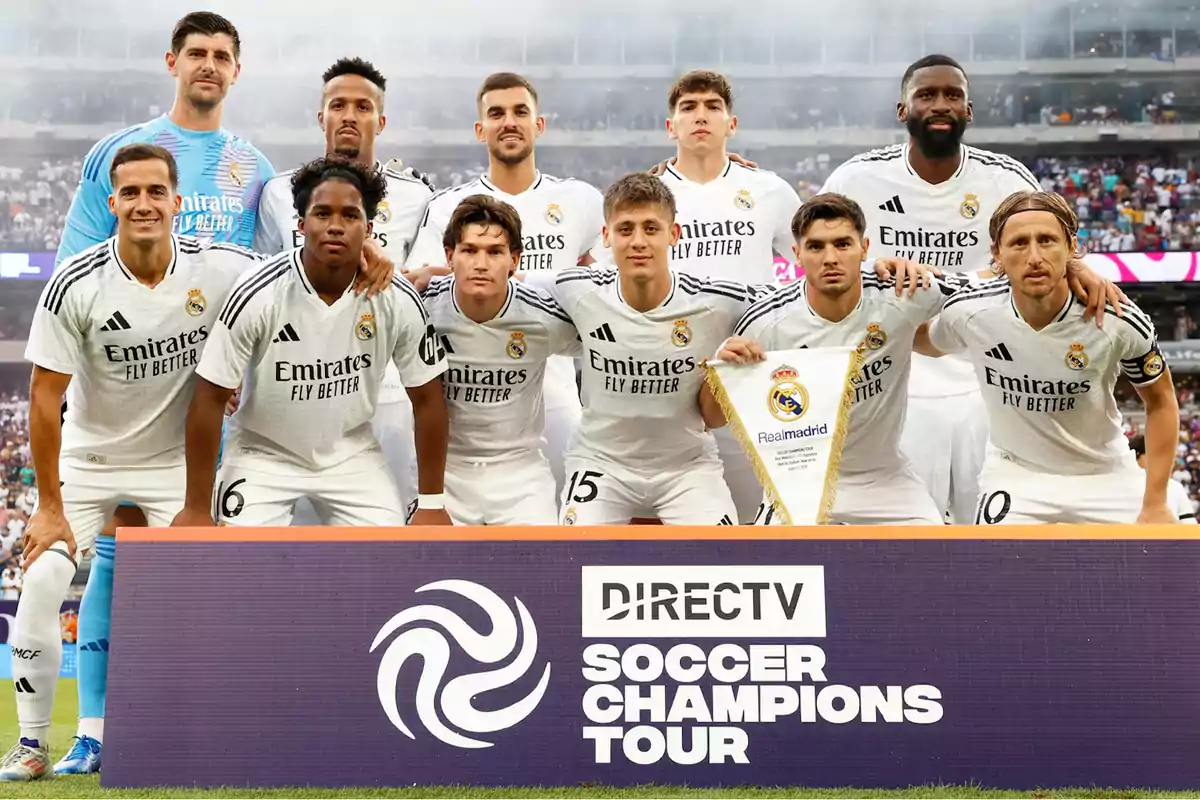 Jugadores del Real Madrid posando para una foto grupal antes de un partido del Soccer Champions Tour, con un cartel de DIRECTV en primer plano.