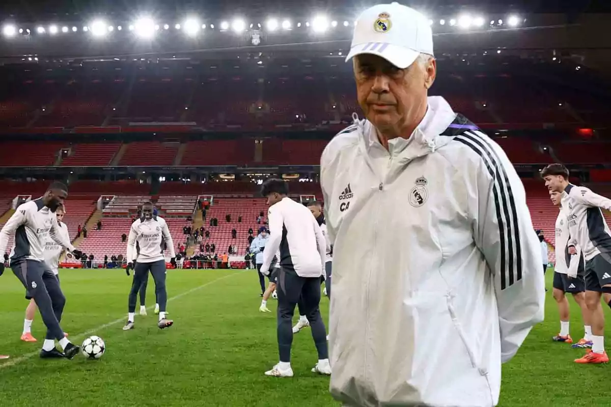 Un entrenador de fútbol con gorra blanca observa a sus jugadores entrenar en un estadio iluminado.