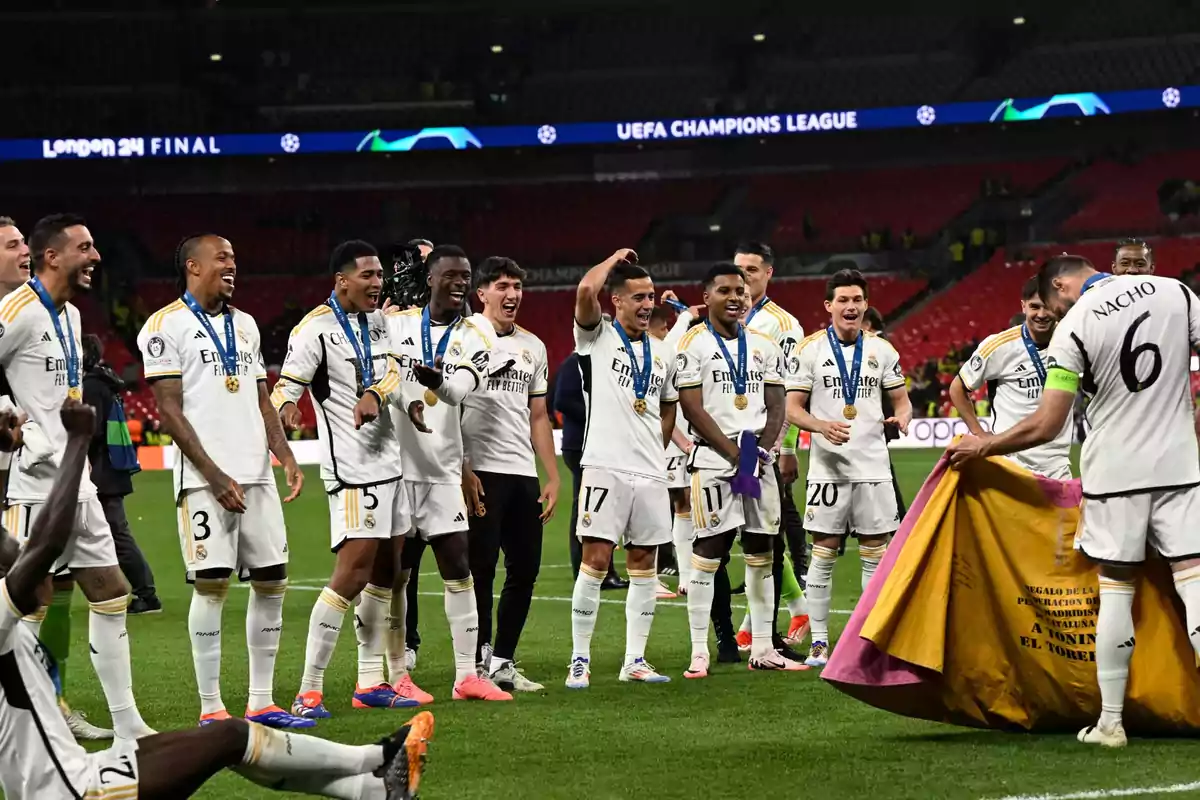 Jugadores de un equipo de fútbol celebran en el campo con medallas alrededor del cuello y una bandera en las manos.