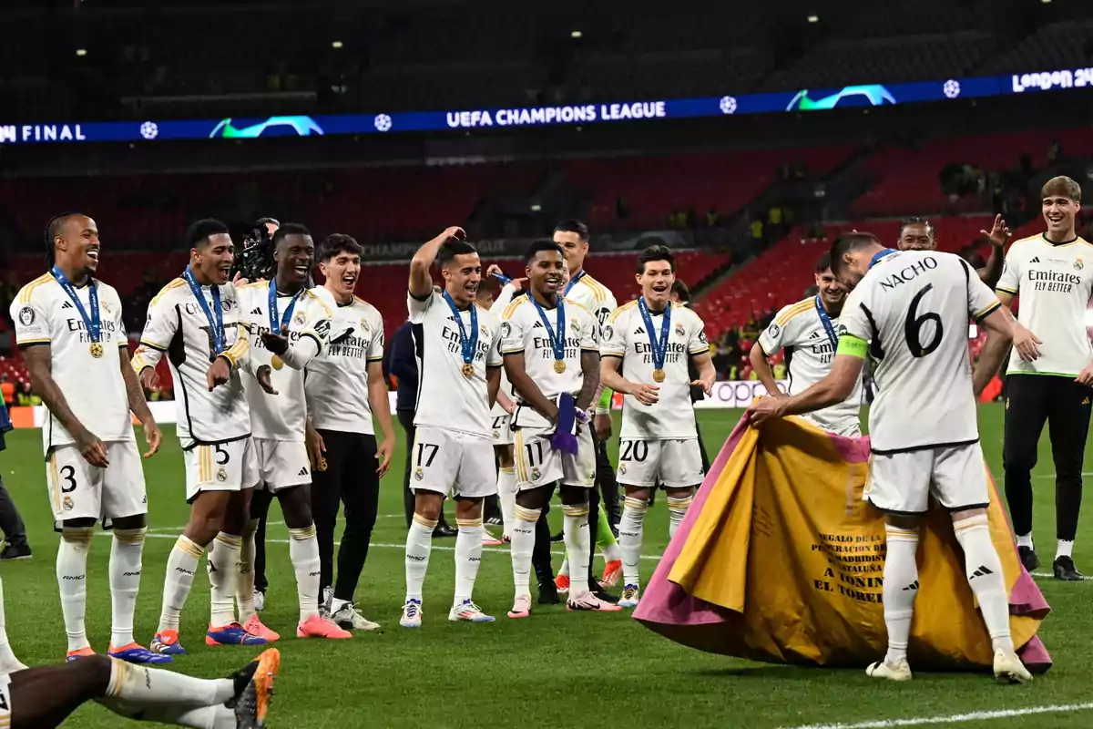 Jugadores de un equipo de fútbol celebran en el campo con medallas alrededor del cuello y uno de ellos sostiene una capa de torero.