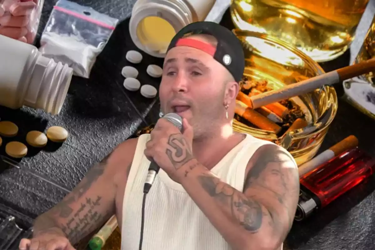 Un hombre con tatuajes y gorra canta con un micrófono en la mano, mientras en el fondo se ven medicamentos, cigarrillos y alcohol.