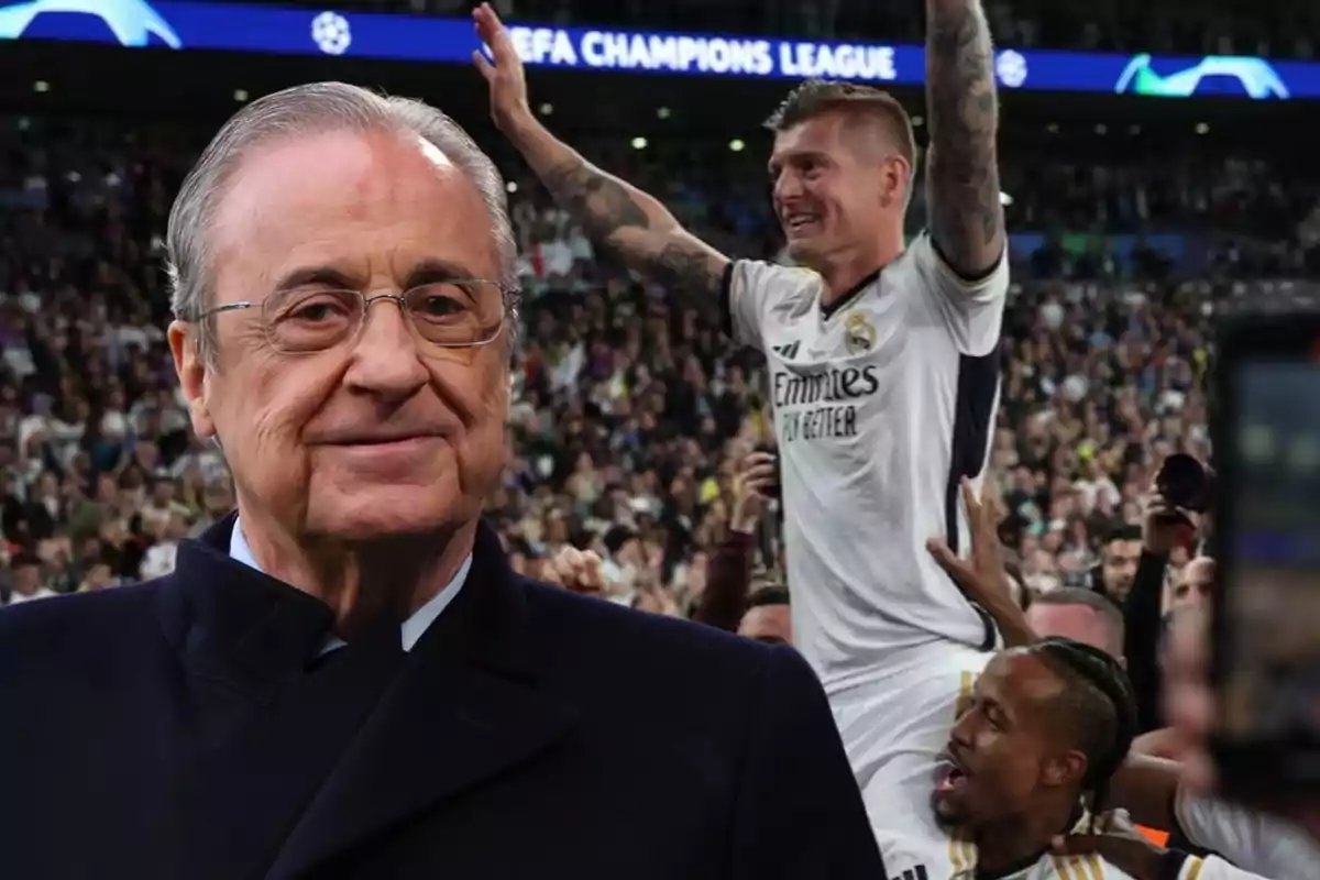 Un hombre mayor con gafas y abrigo oscuro está en primer plano mientras un jugador de fútbol celebra con los brazos en alto en el fondo de un estadio lleno de espectadores.