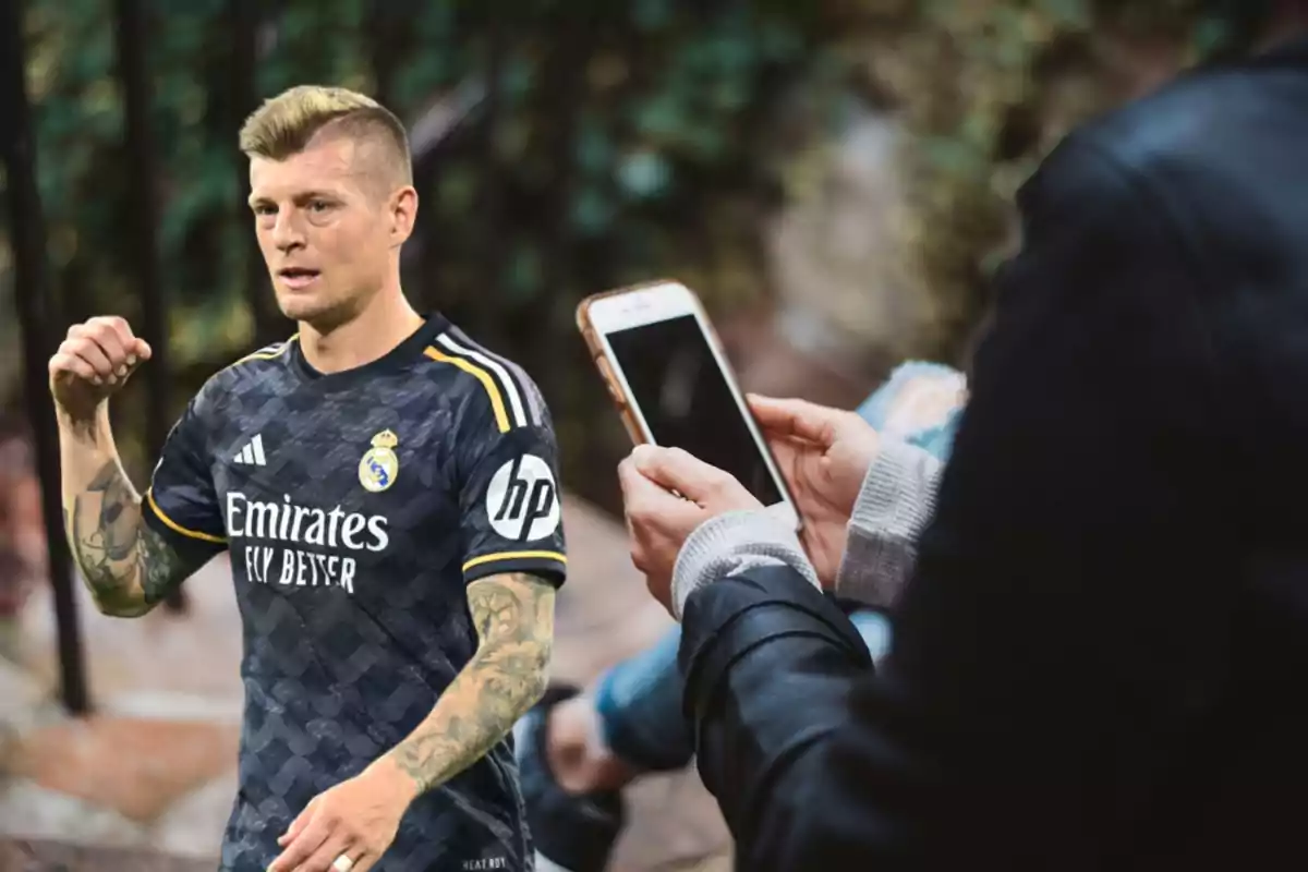 Un jugador de fútbol con uniforme del Real Madrid es fotografiado por una persona con un teléfono móvil.