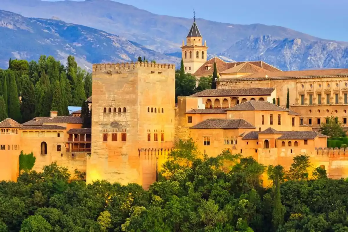 Vista de la Alhambra de Granada con montañas al fondo y rodeada de vegetación.