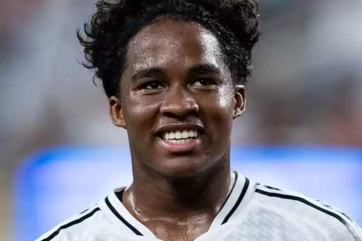 Jugador de fútbol sonriente con camiseta blanca y negra.