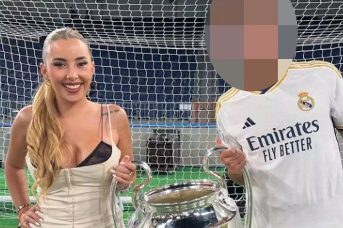 Dos personas posando con un trofeo de fútbol frente a una portería, una de ellas con una camiseta del Real Madrid.