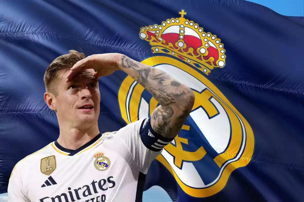 Un jugador de fútbol con el uniforme del Real Madrid se cubre los ojos con la mano, con una bandera del equipo de fondo.