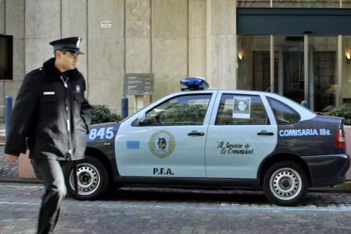 Policía caminando junto a un patrullero de la Policía Federal Argentina estacionado frente a un edificio Policía caminando junto a un patrullero de la Policía Federal Argentina estacionado frente a un edificio